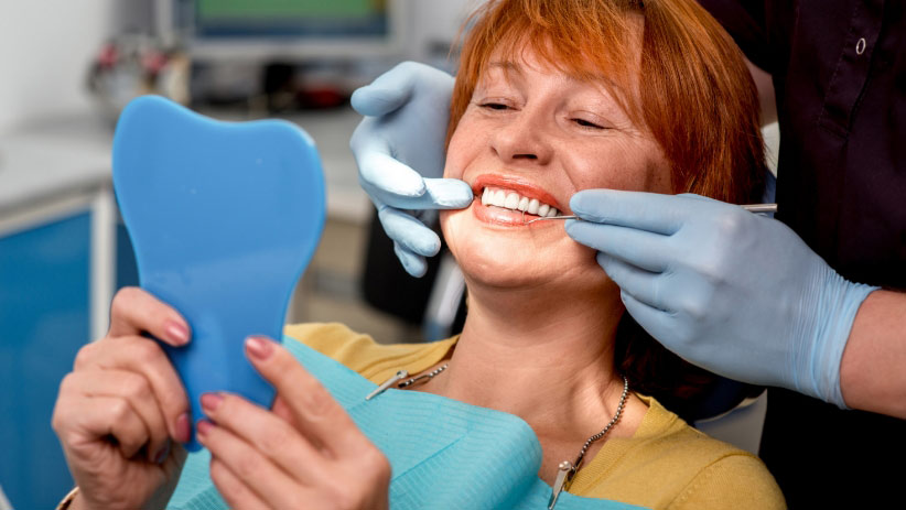 Female Dentist Viewing Patient Teeth In Dental Mirror